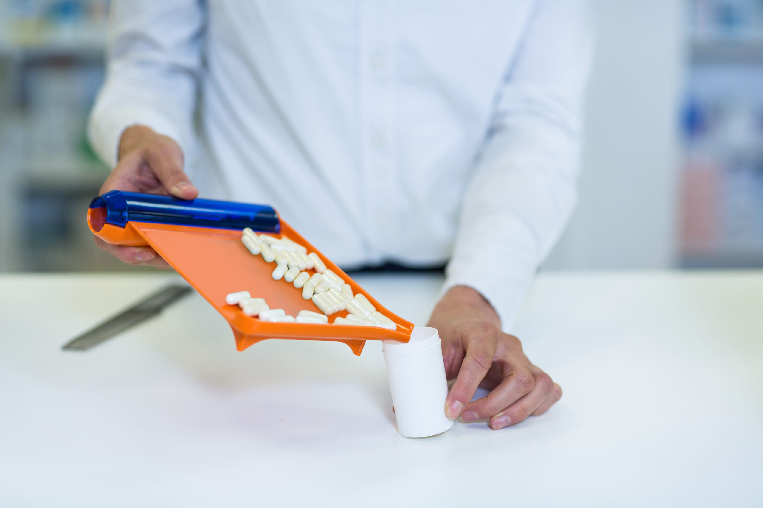 Mid-section of pharmacist putting pill in container at pharmacy